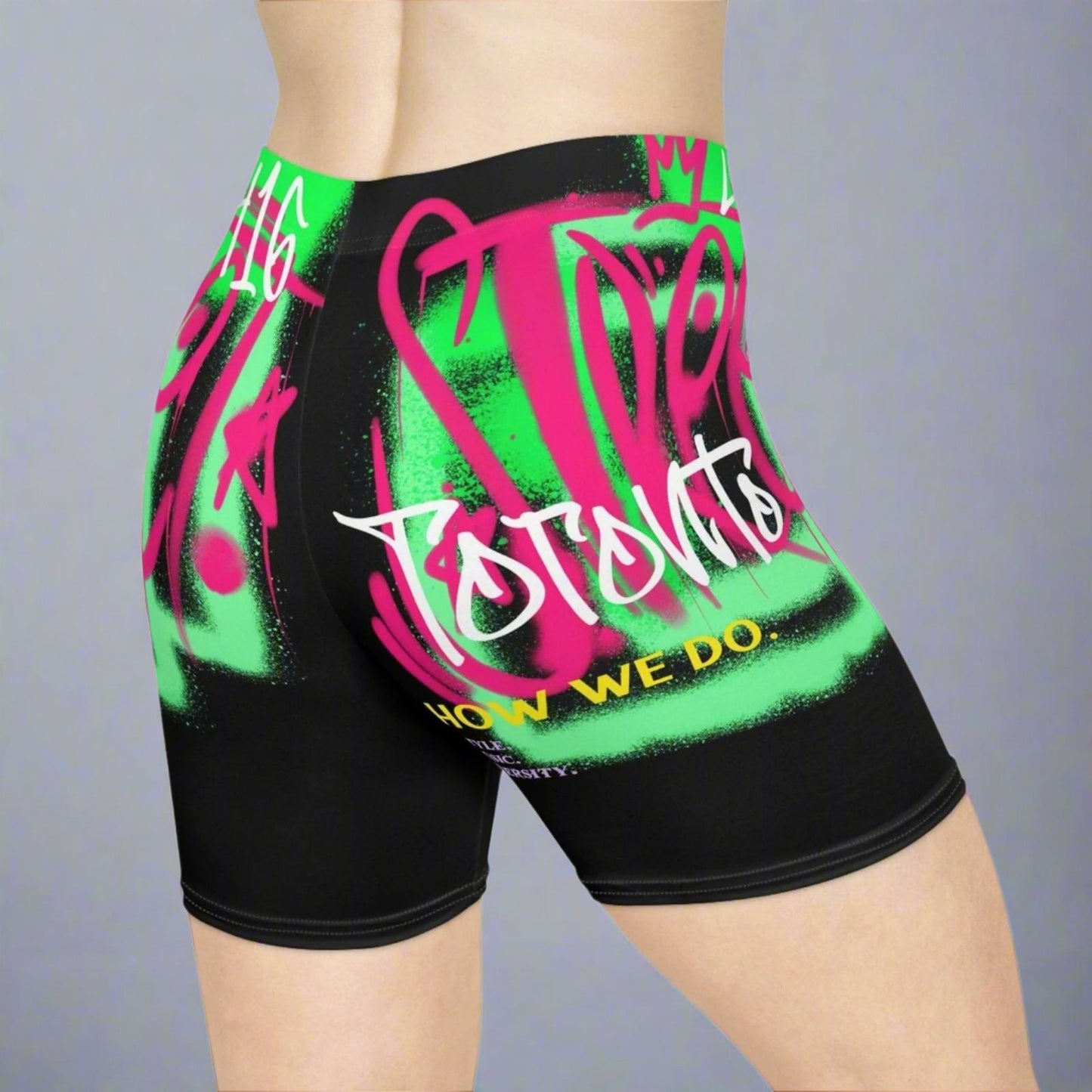 90s Black, neon green and neon pink biker shorts with text about Toronto and graffiti graphics worn in front of a gray background | Ohhh So Swag