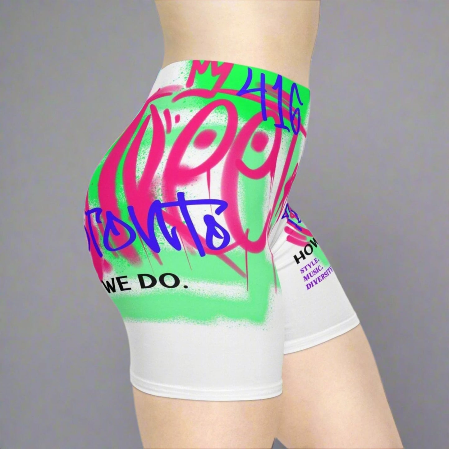 Close up view of woman wearing colorful graffiti Toronto white biker shorts with blue, neon green and neon pink in front of a gray background | Ohhh So Swag
